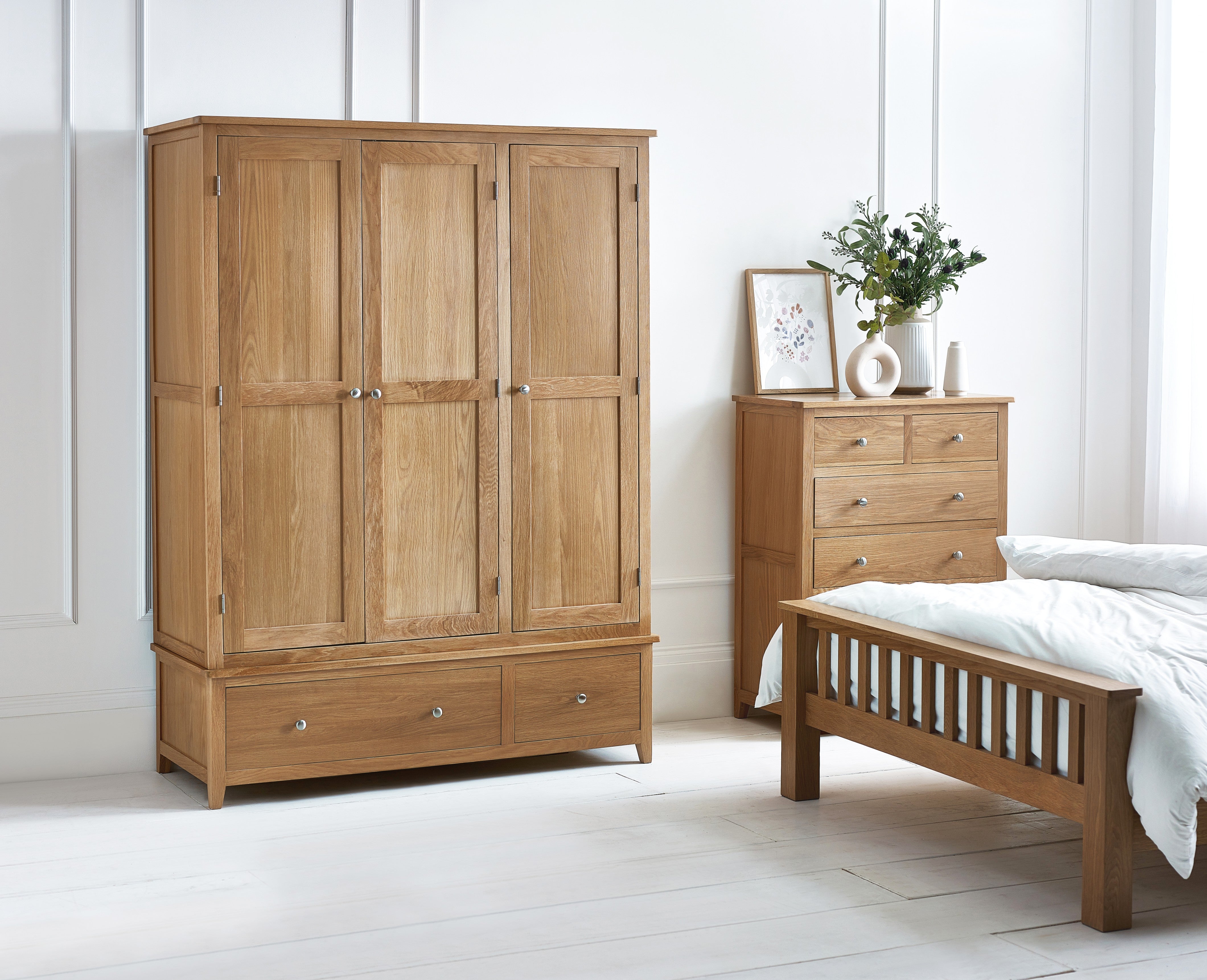 Wooden wardrobe, bed, and dresser in a bedroom setting with white walls and floor.