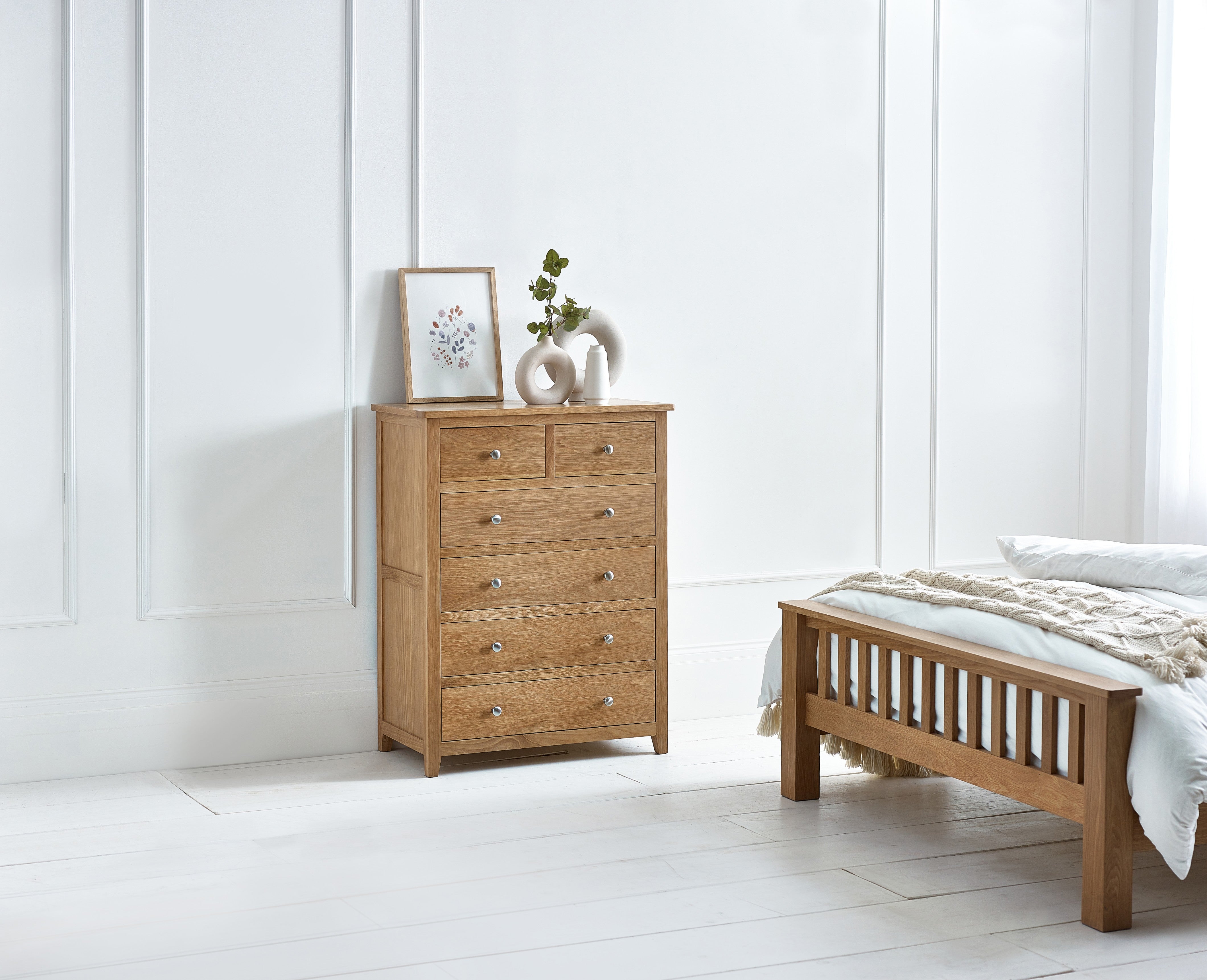 Wooden dresser and bed in a bedroom with white walls and flooring