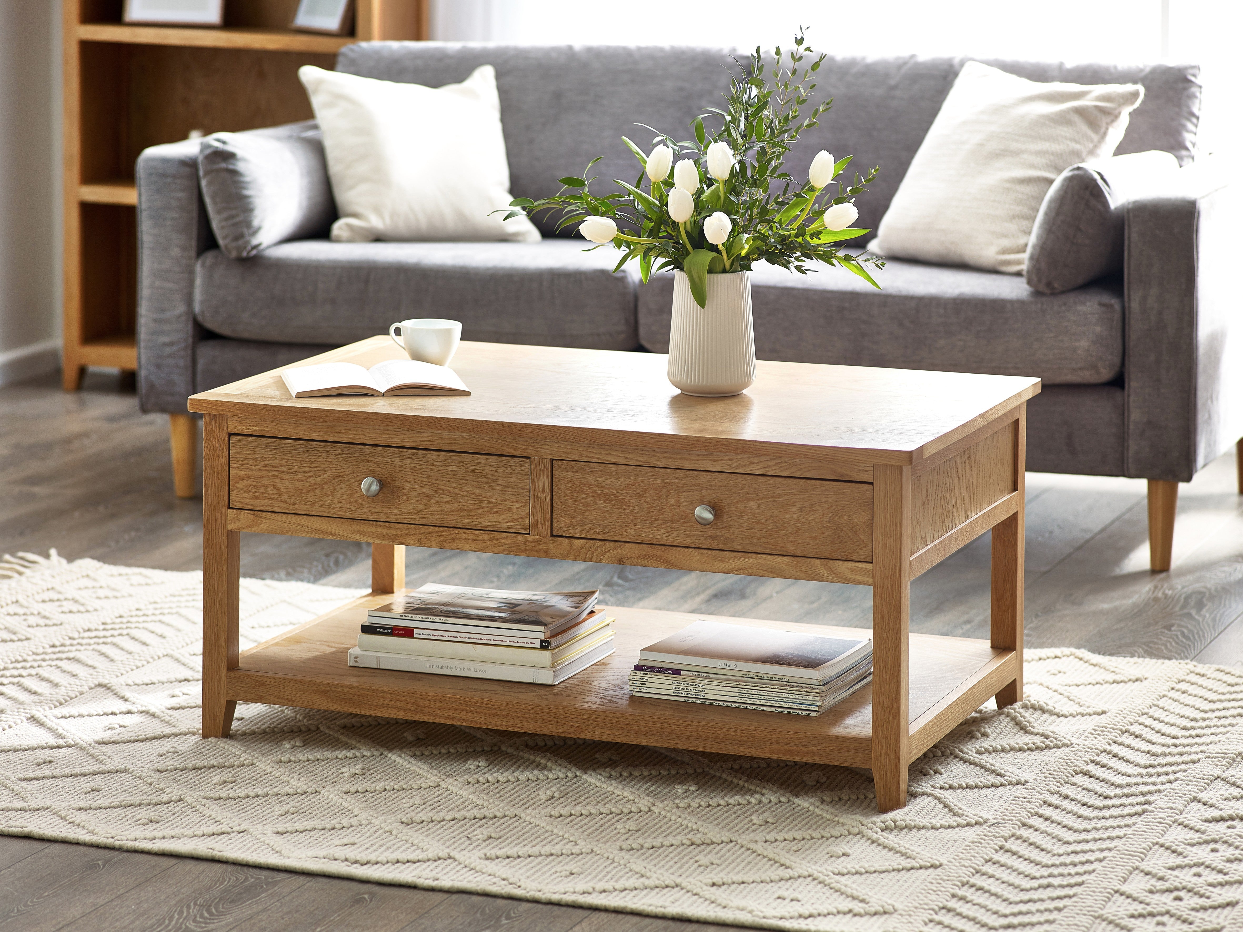 Wooden coffee table with books and a vase of flowers in front of a gray sofa.