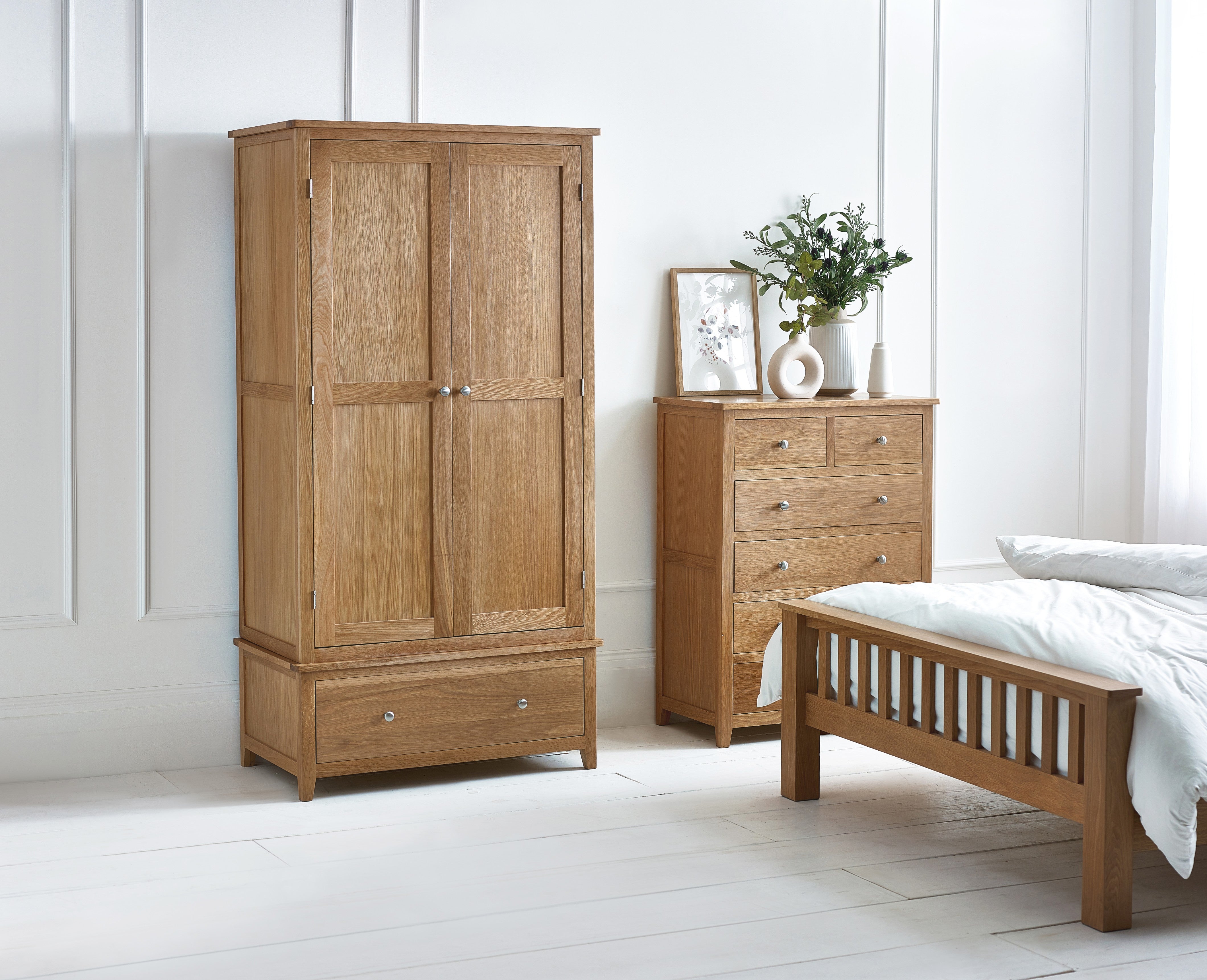 Wooden wardrobe, bed, and dresser in a bedroom setting with white walls and floor.