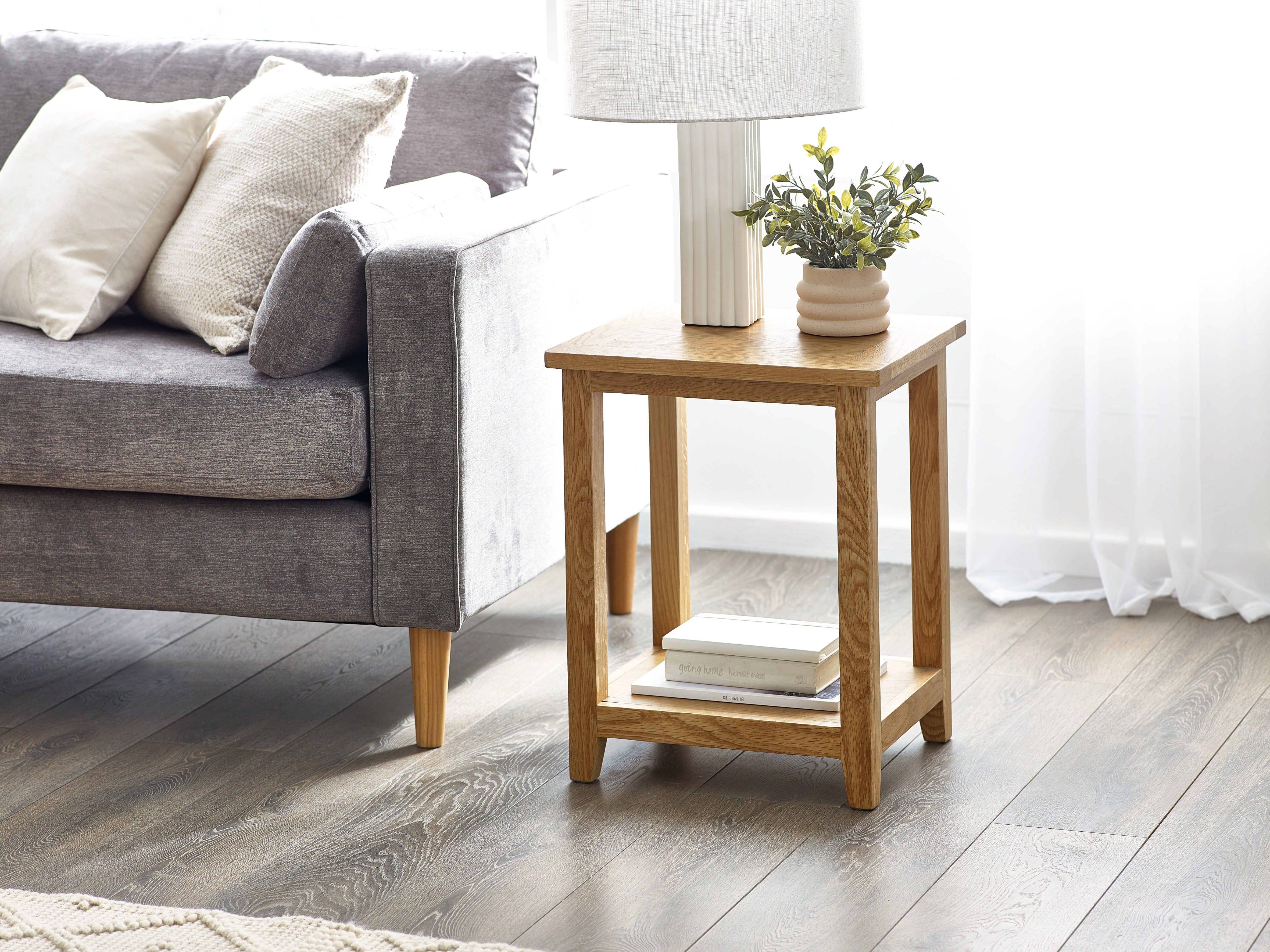 Wooden side table with lamp and books next to a gray sofa in a living room.