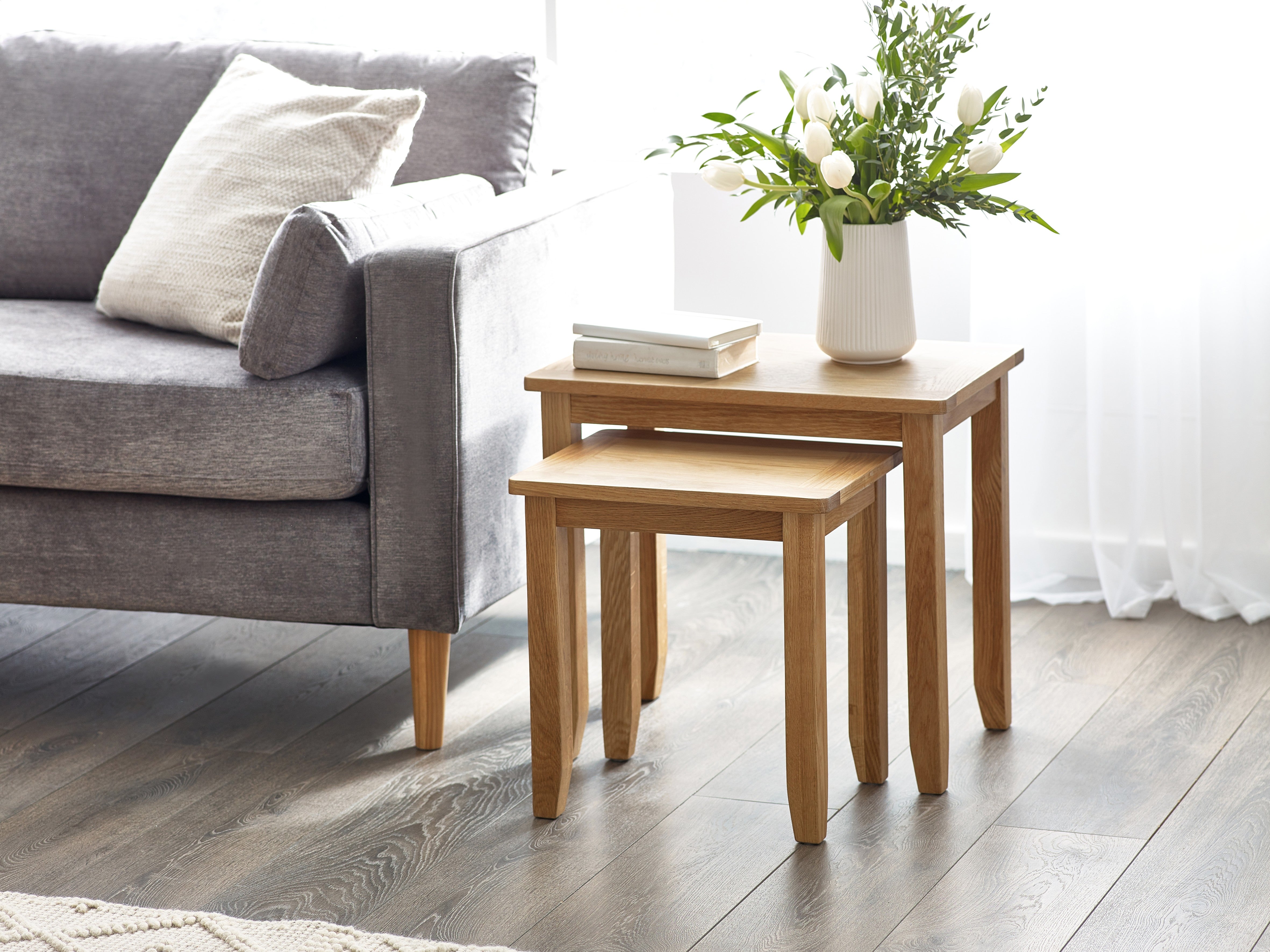 Nest of wooden tables in a living room setting with a gray sofa and decorative items.