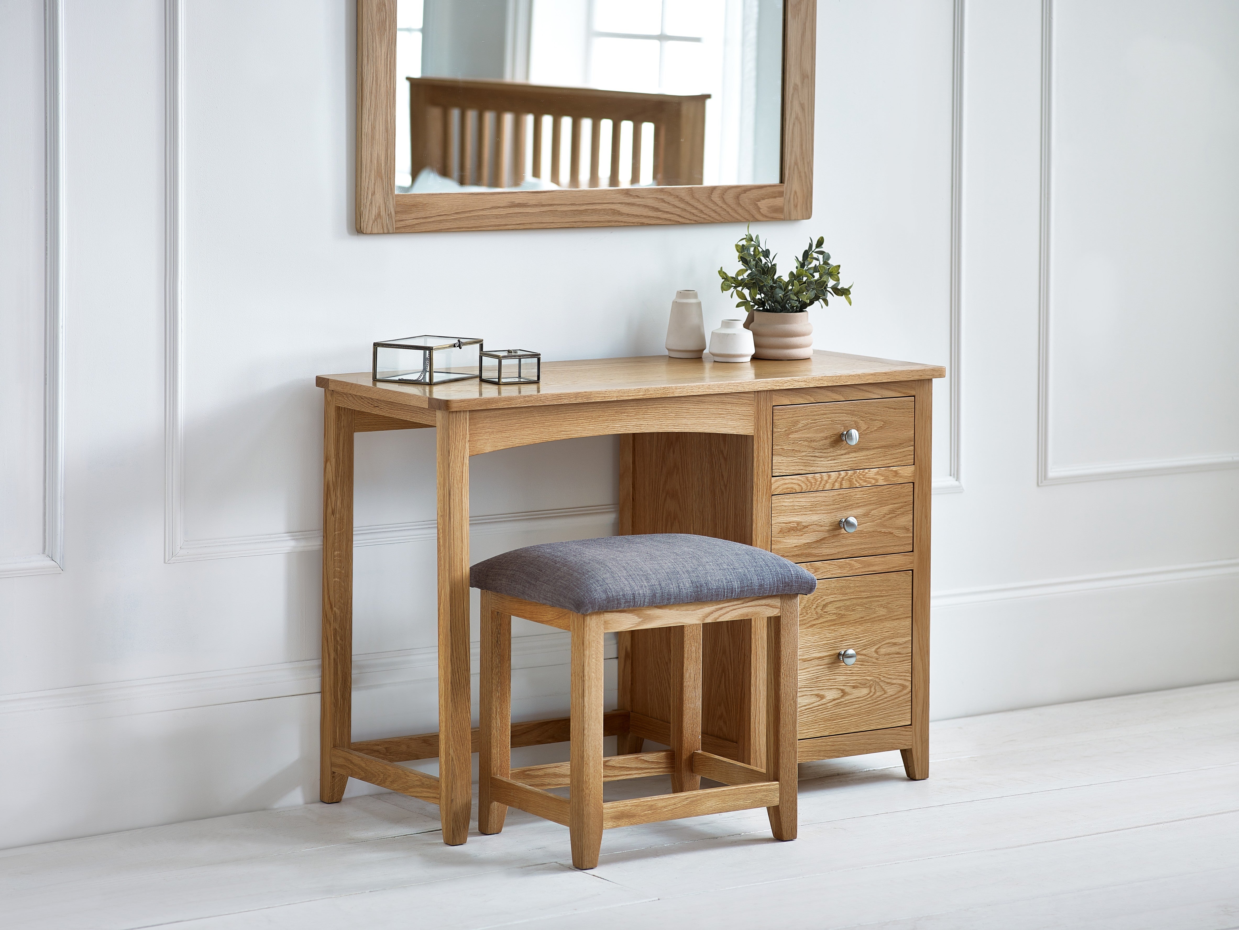 Wooden dressing table with mirror, stool, and decorative items in a bright room.