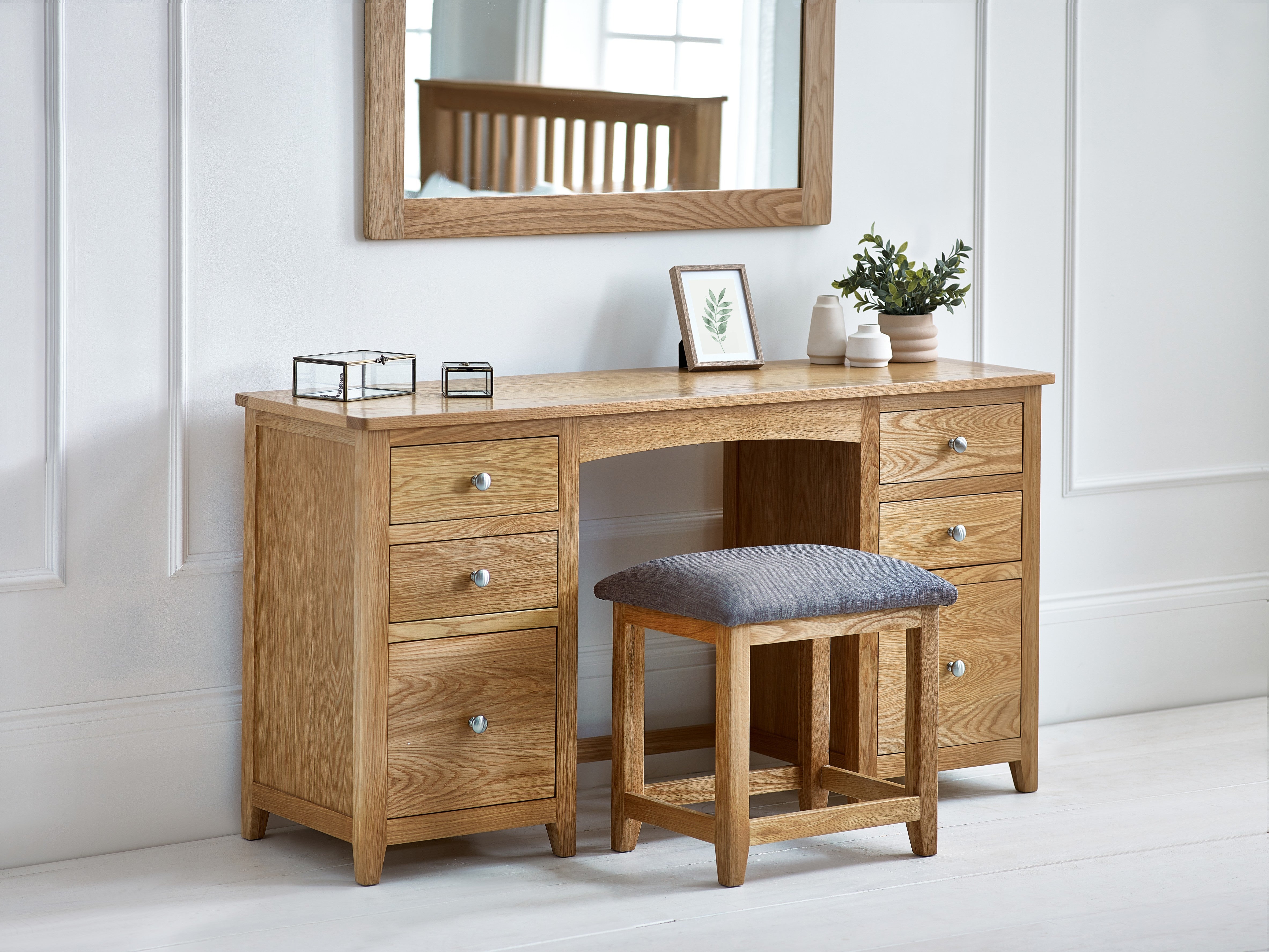 Wooden dressing table with mirror, stool, and decorative items in a room.
