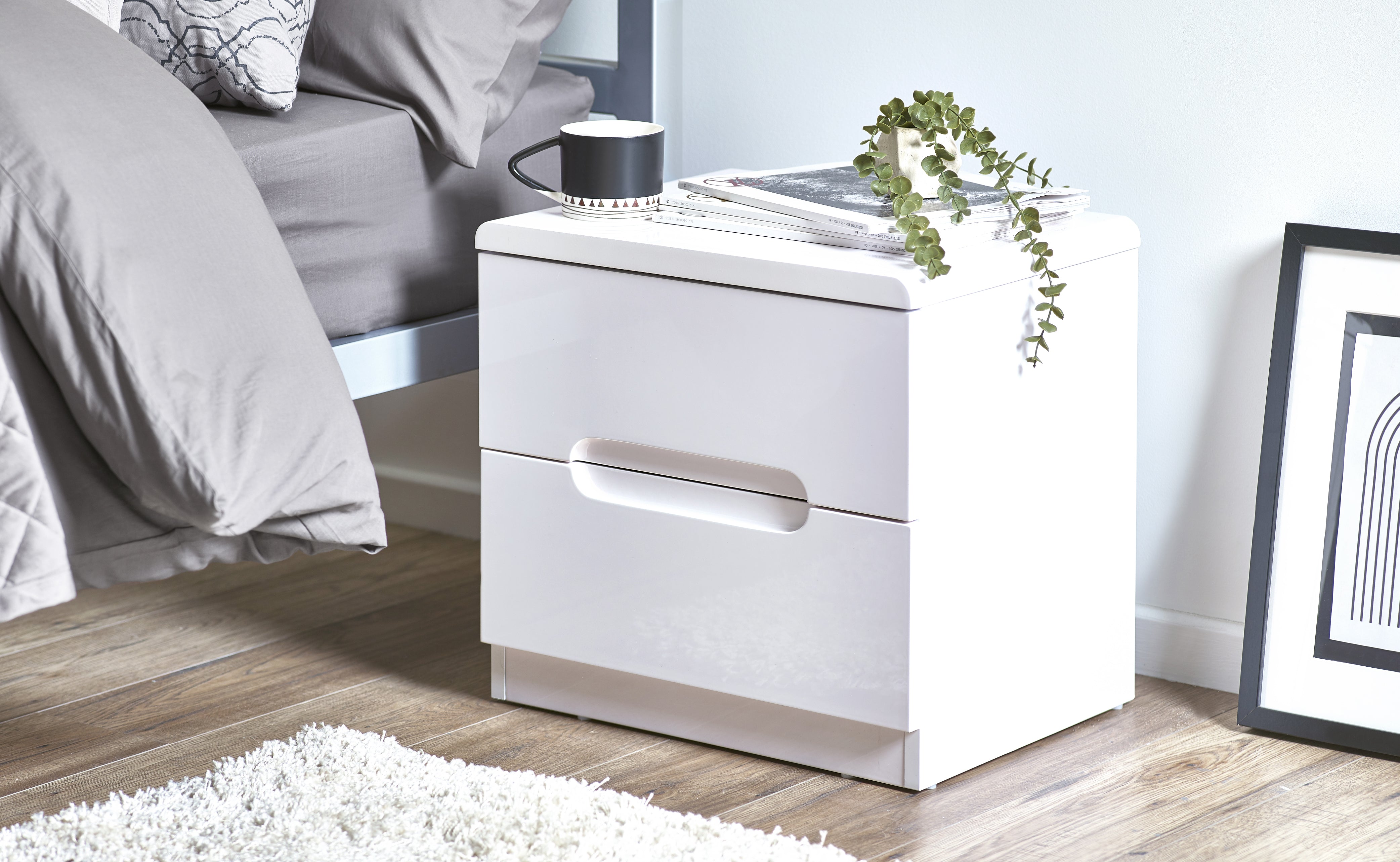 White nightstand with a lamp and plant in a bedroom setting