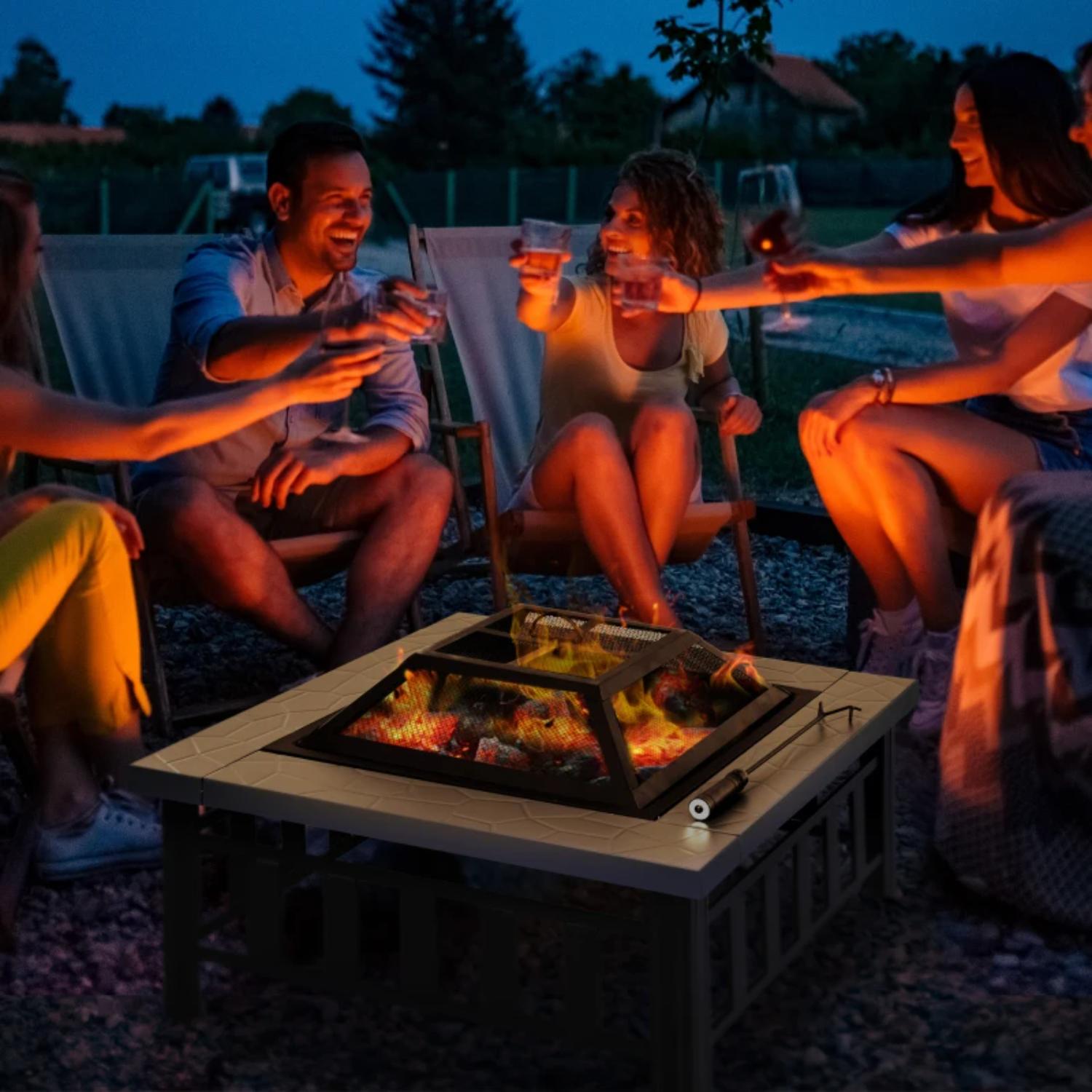 Group of people sitting around a fire pit at night, toasting with glasses.