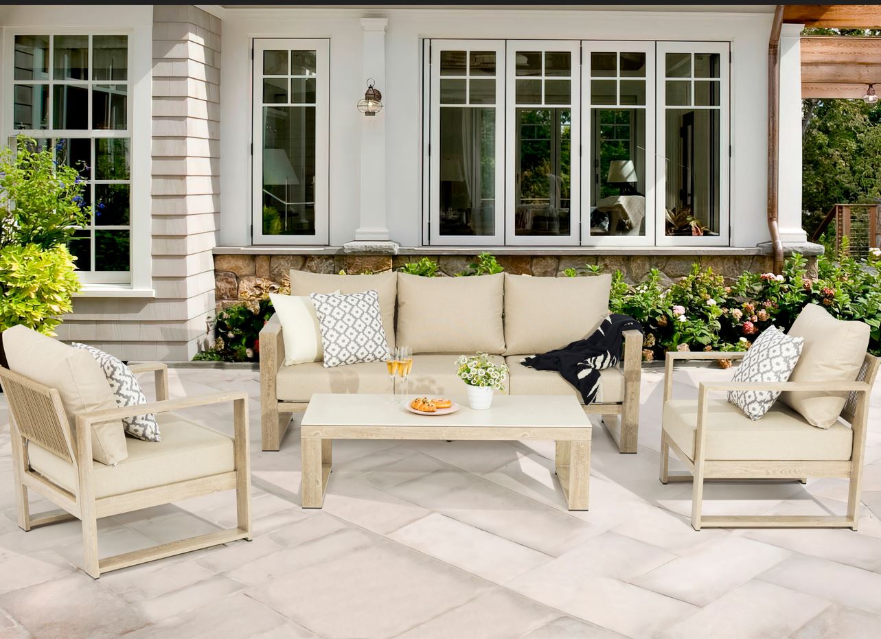 Outdoor patio set with beige furniture and cushions in front of a house.
