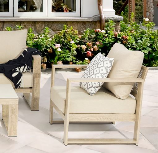Outdoor patio furniture set with beige chairs and cushions on a patio with flowers in the background.