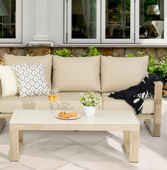 Beige outdoor sofa with cushions, a coffee table, and decorative items on a patio.