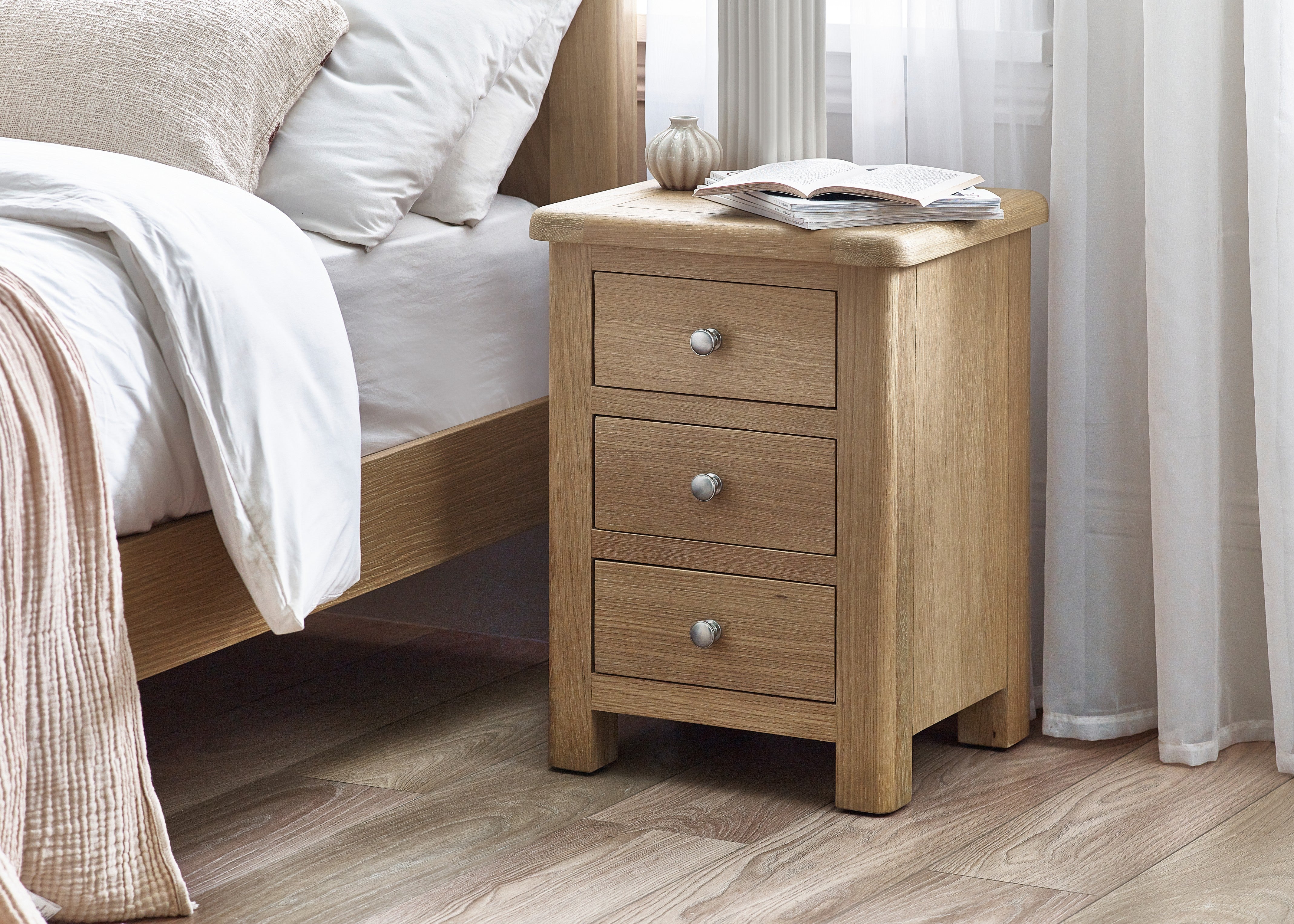 Wooden nightstand with two drawers next to a bed with white bedding.