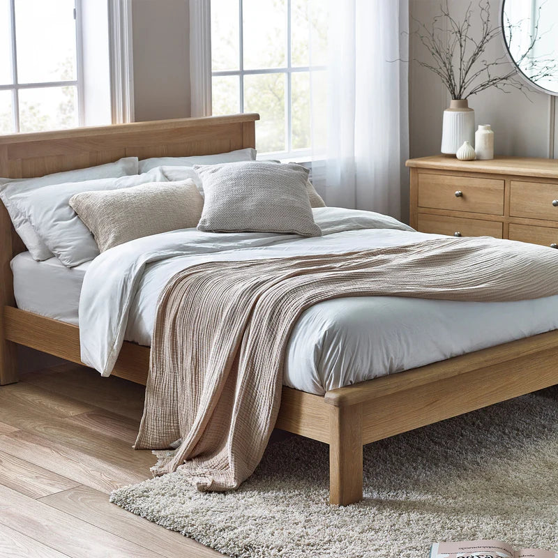 Wooden bed with white bedding and a beige throw blanket in a bright bedroom.