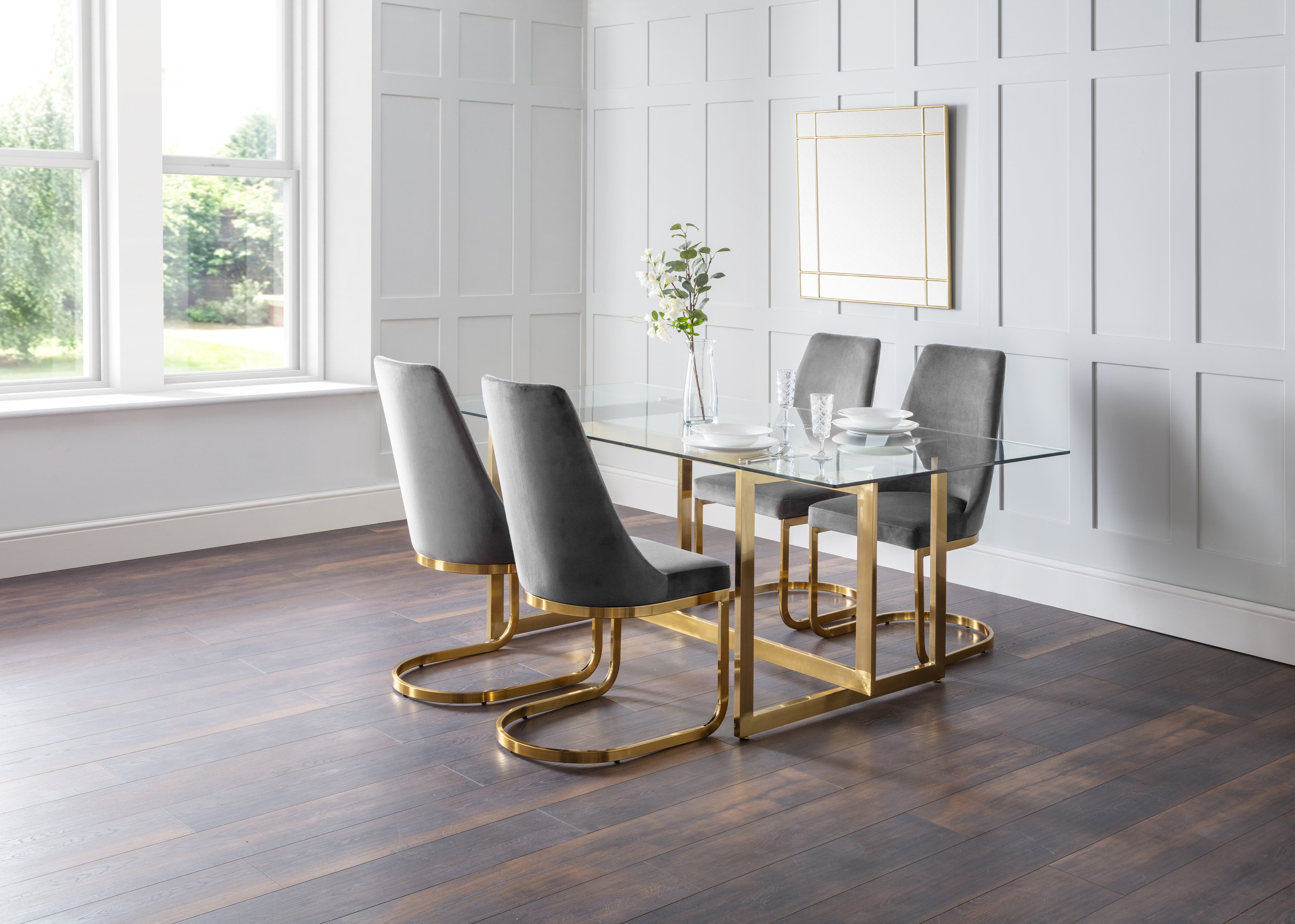 Dining room with a glass table and gray chairs on a wooden floor.