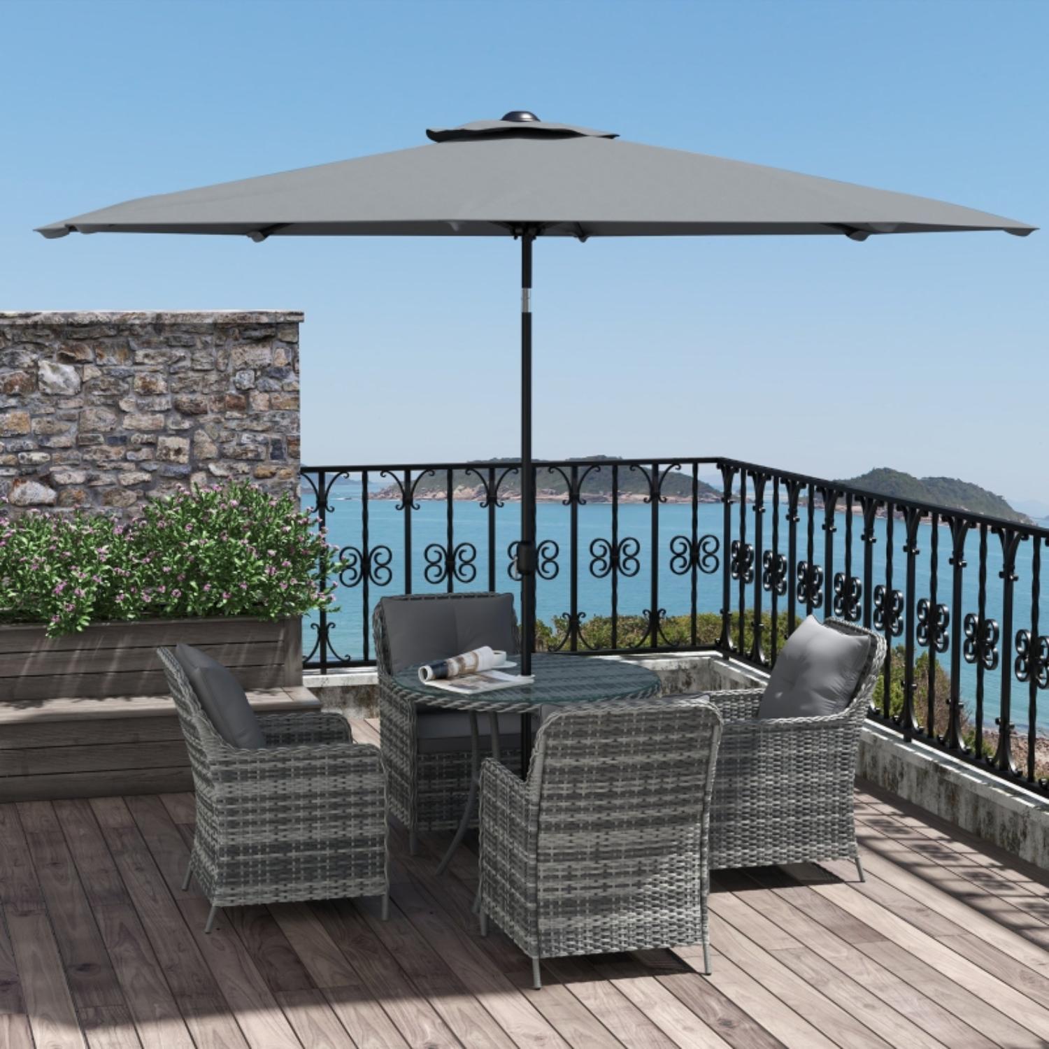 Outdoor patio set with table and chairs under a large umbrella on a deck with ocean view.