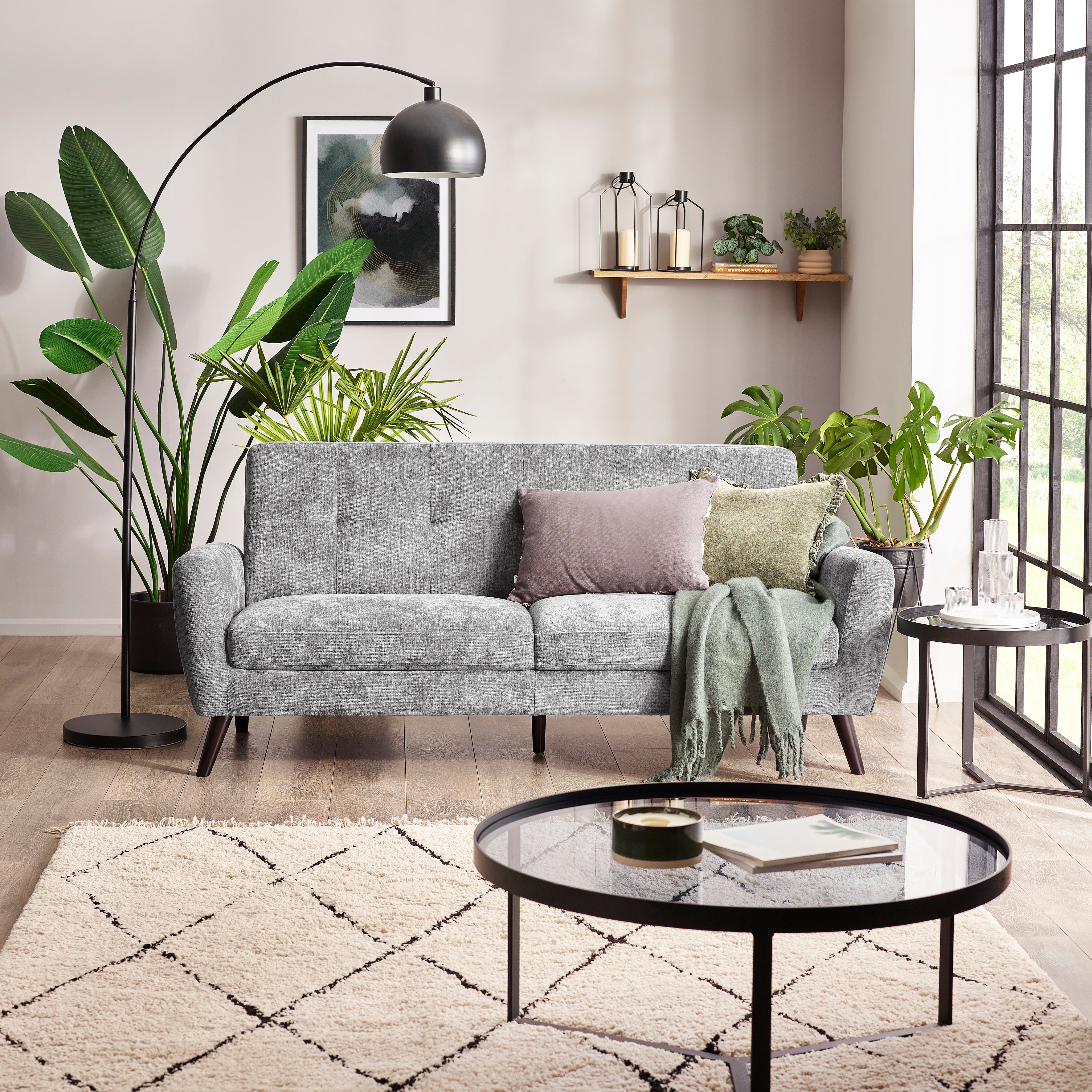 Modern living room with a gray sofa, round glass coffee table, and decorative plants.
