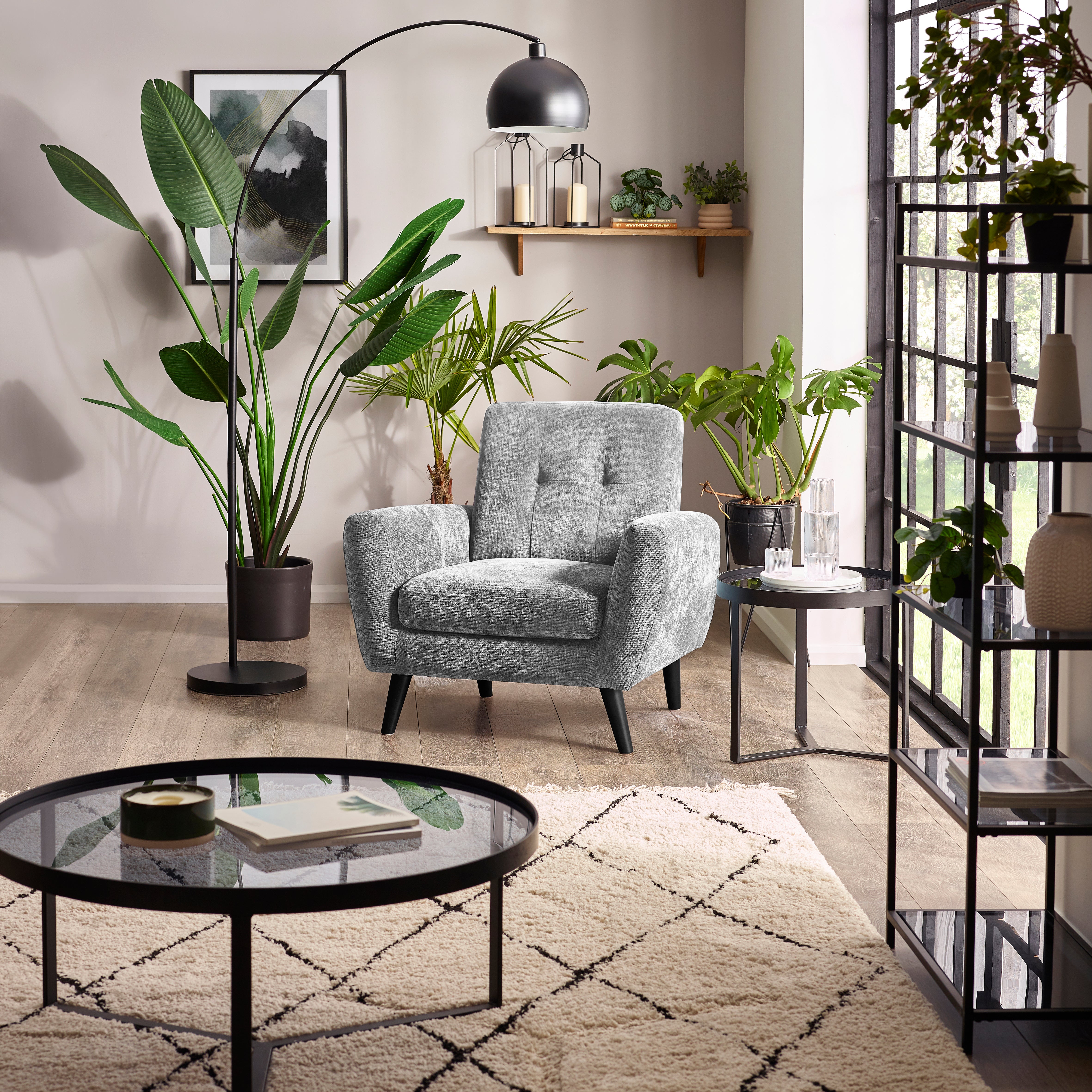 Modern living room with a gray armchair, round glass coffee table, and decorative plants.