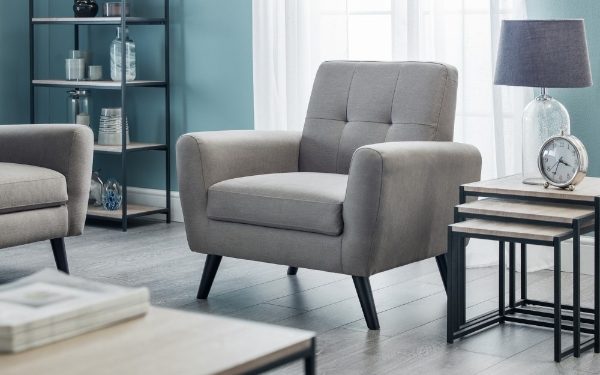 Gray armchair in a living room setting with a lamp and shelves in the background.