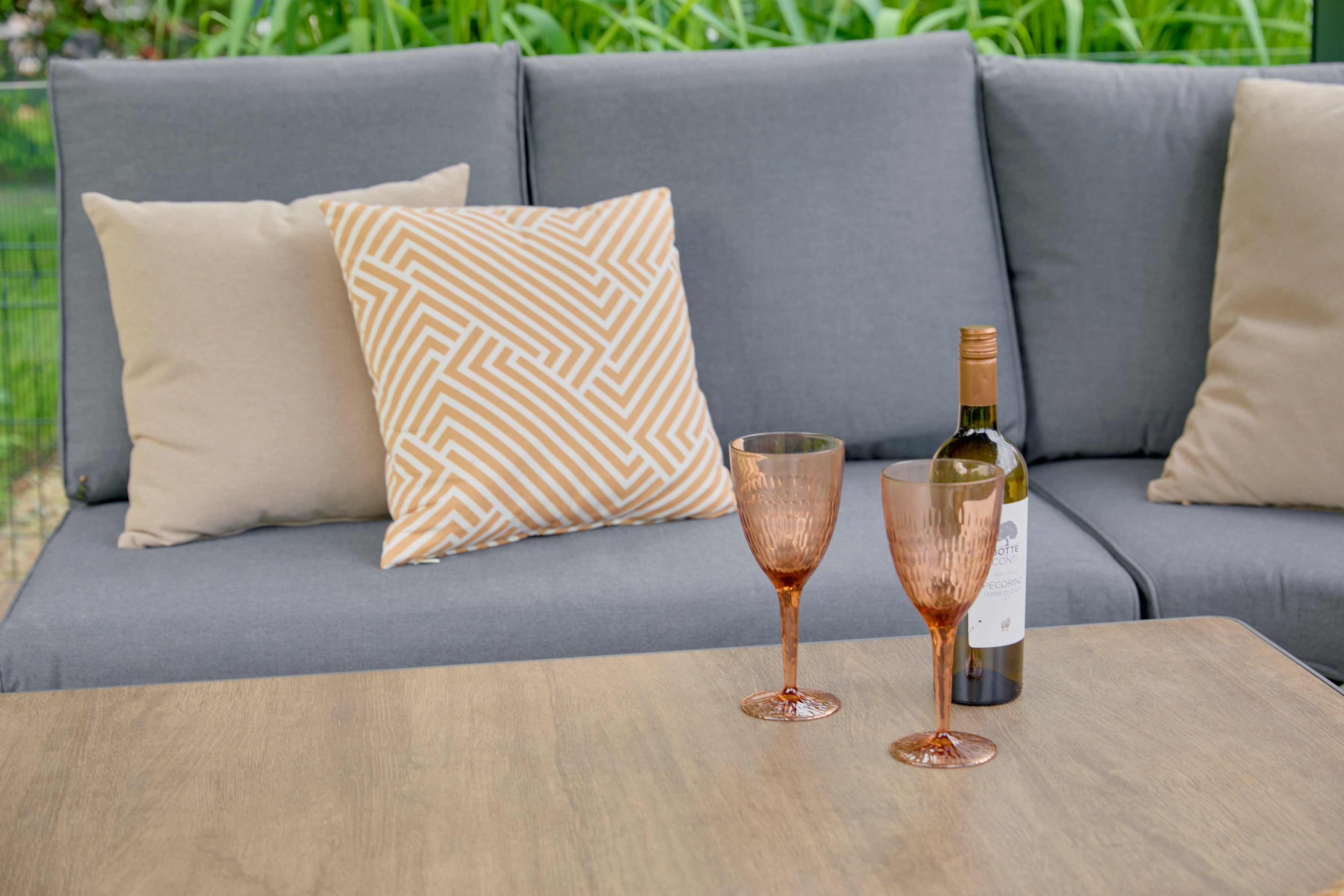 Gray outdoor sofa with patterned cushions and a bottle of wine on a table.