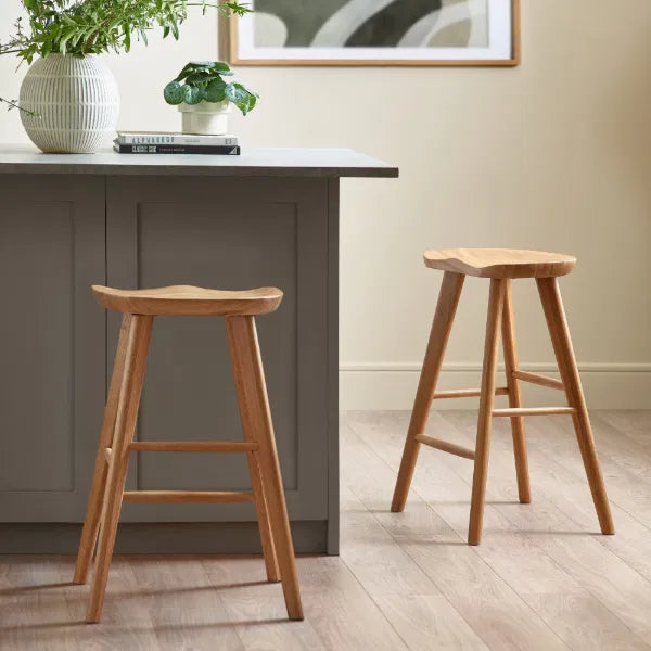 Two wooden bar stools in front of a gray kitchen island with a plant and books on top.
