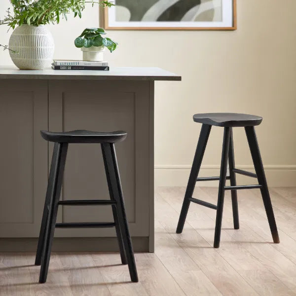 Two black bar stools in front of a gray dining table with a plant and books on it.