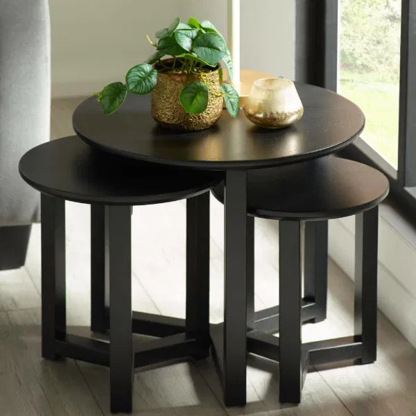 Set of three black nesting tables with decorative items on a light wood floor.