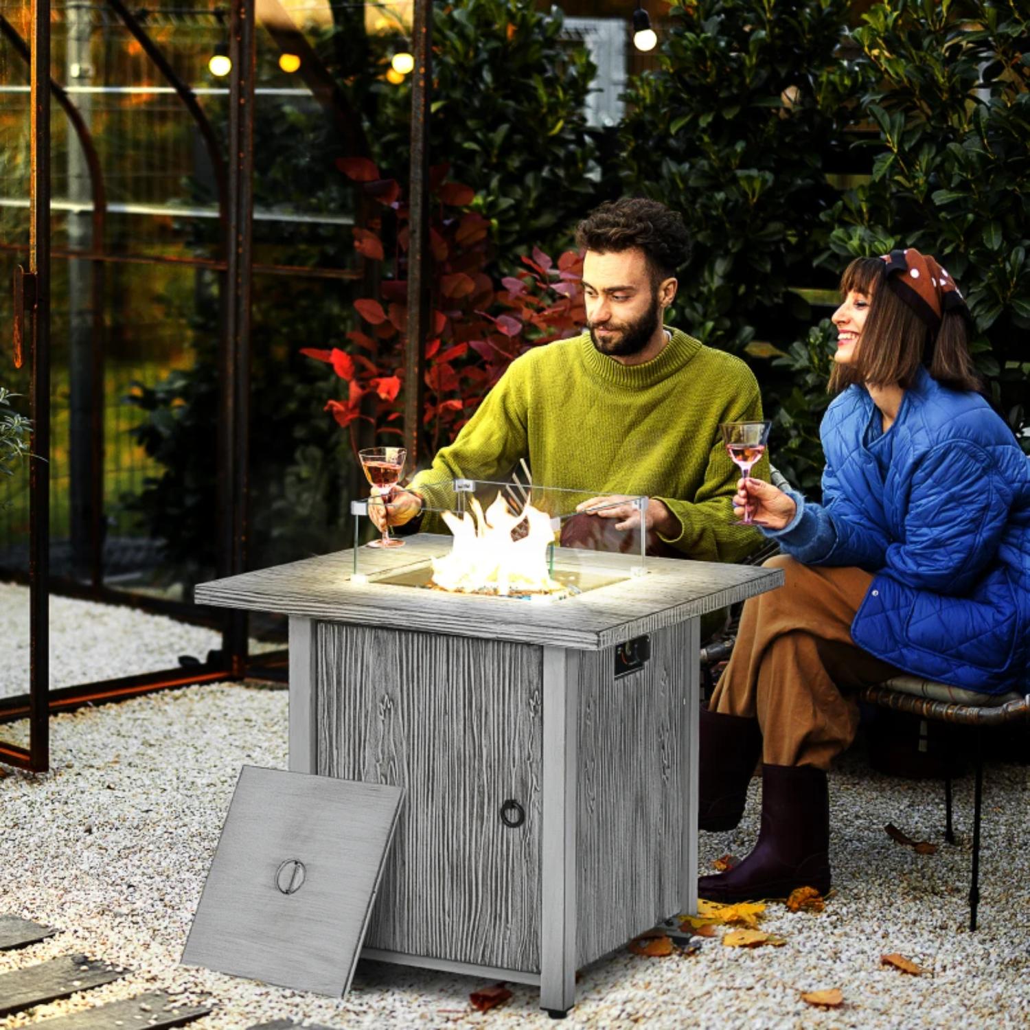 Two people sitting around a fire pit table in an outdoor setting.