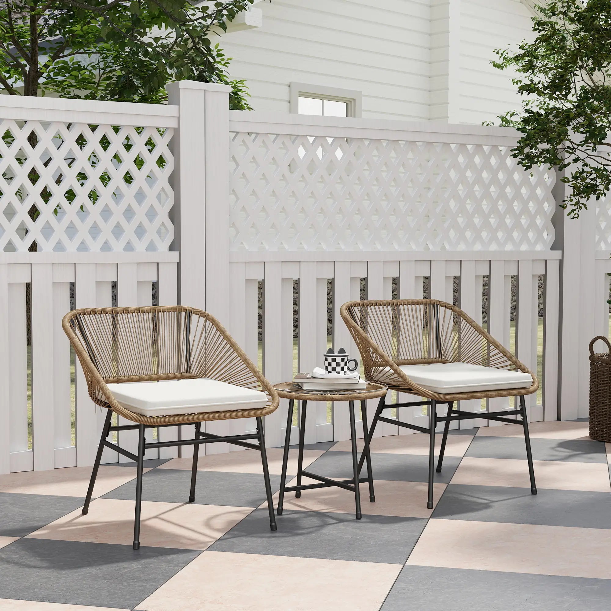 Two wicker chairs with cushions and a small table on a patio with a white lattice fence and trees in the background.