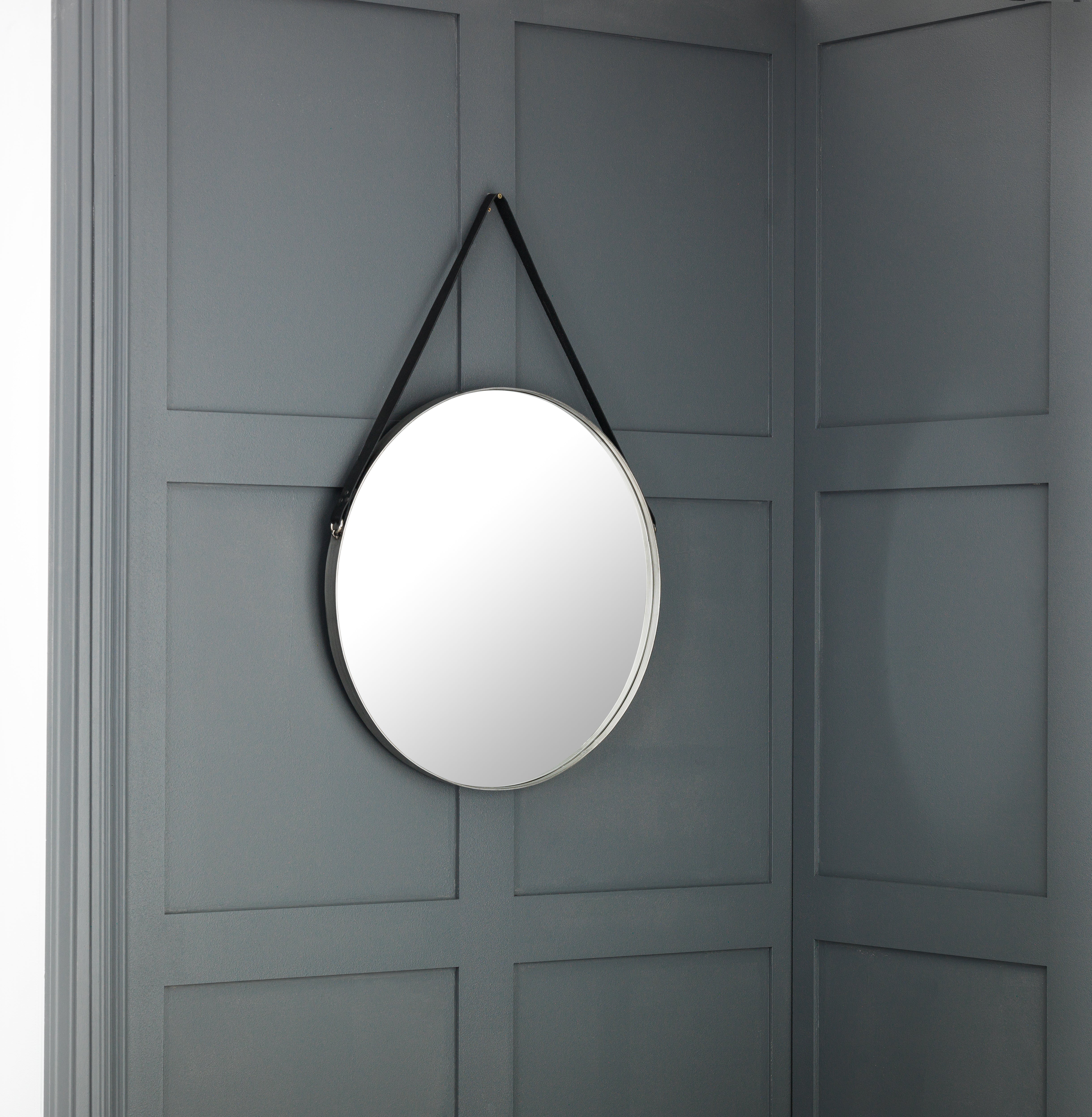 Round mirror with black strap hanging on a gray paneled wall