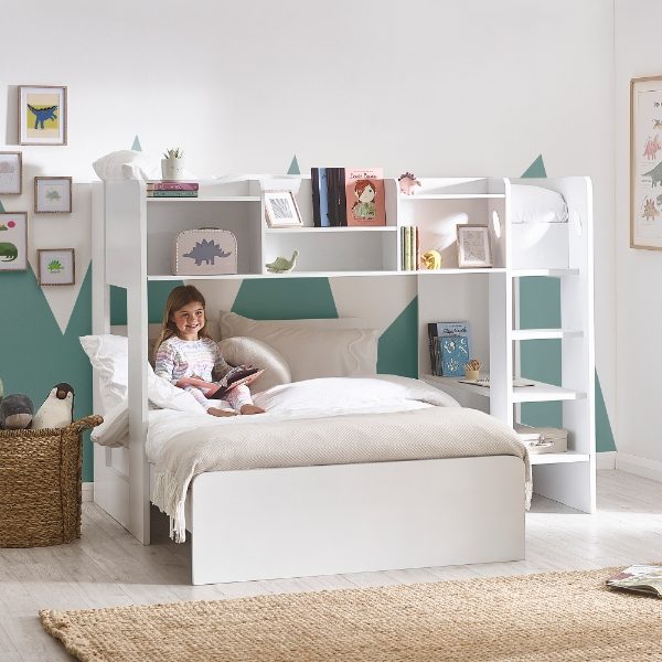 Child reading a book in a white bed with bookshelves in a room with green walls and decorative elements.