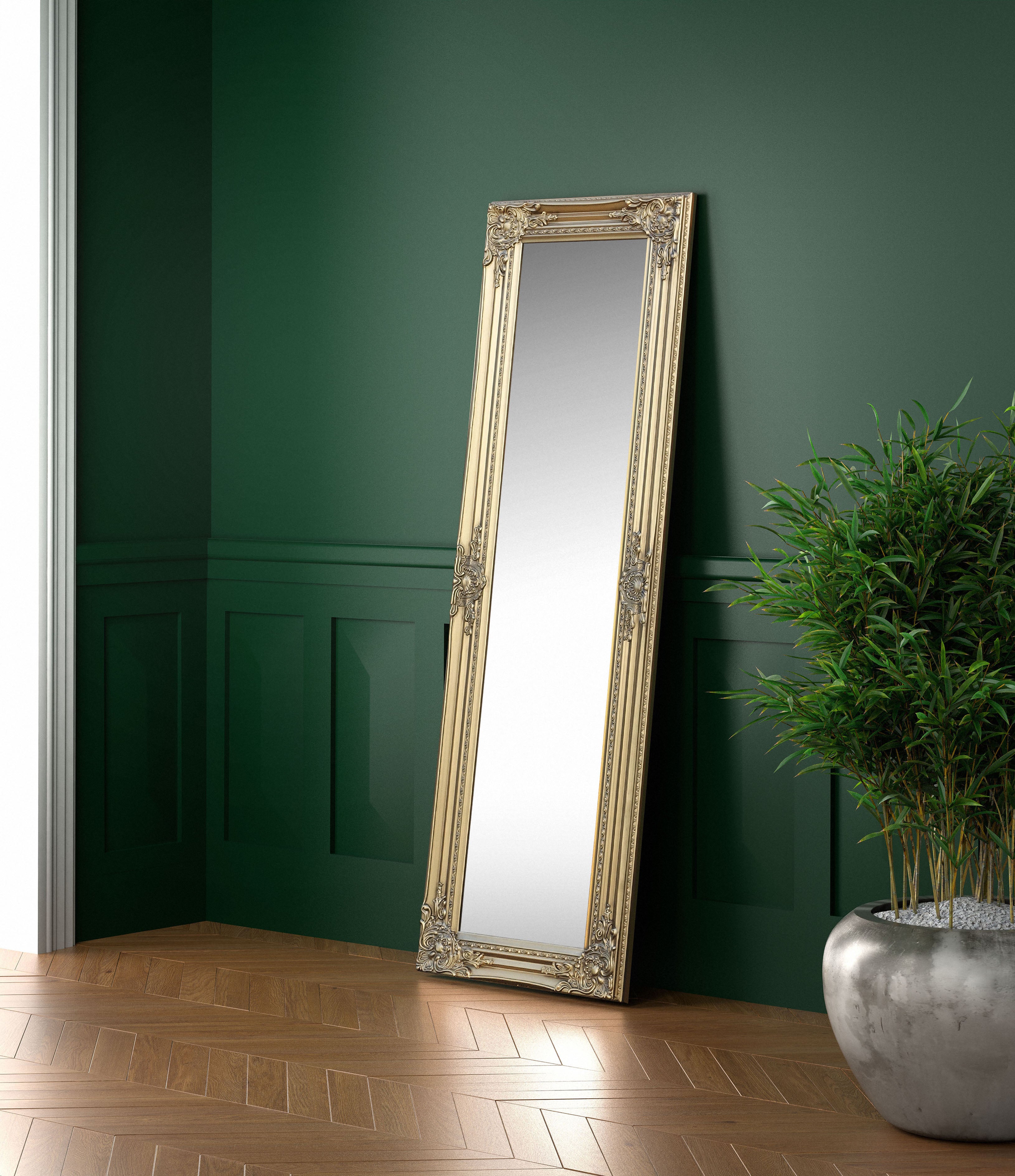 Decorative floor mirror with gold frame against a green wall