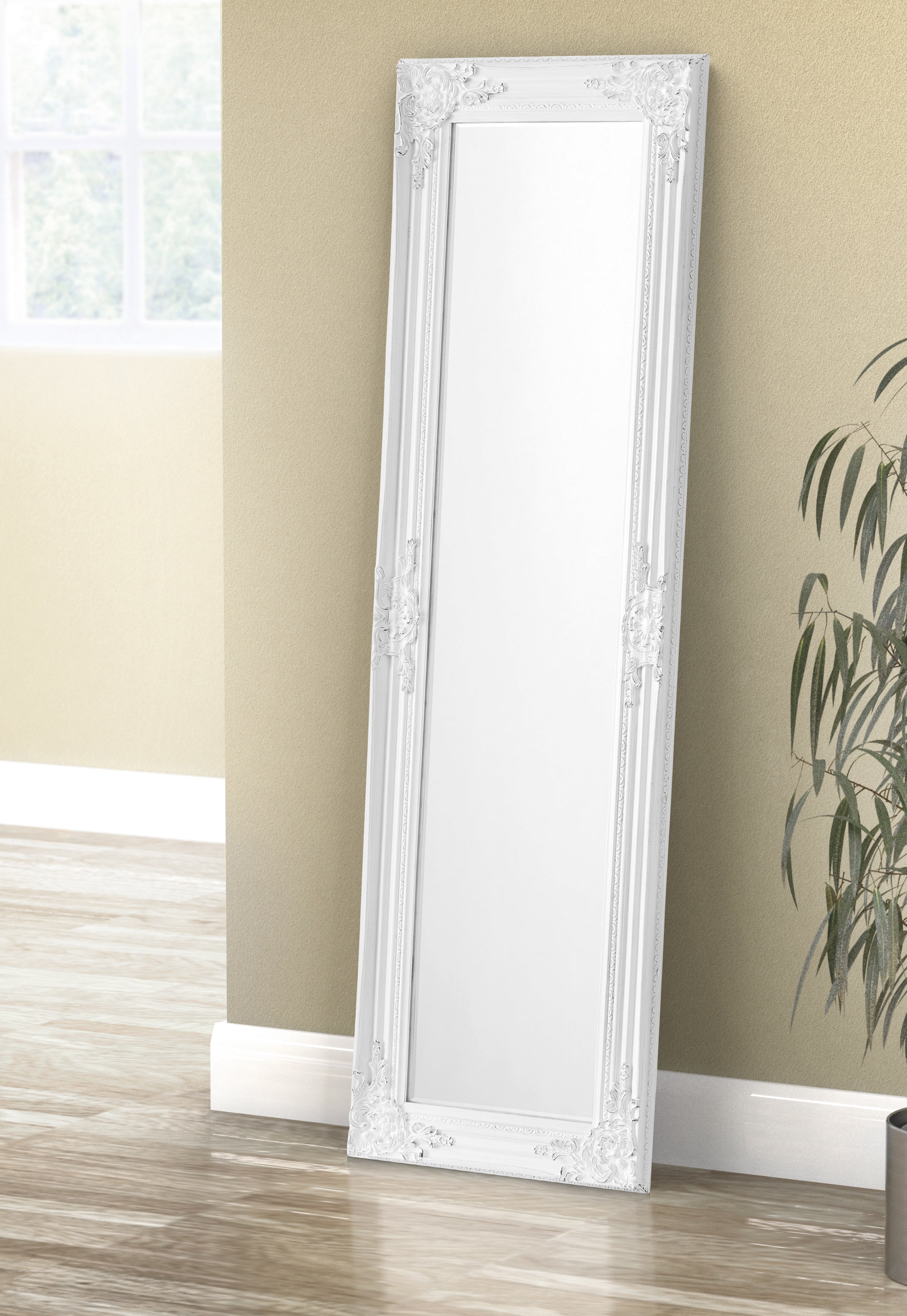 White decorative mirror leaning against a beige wall with a plant in the corner.