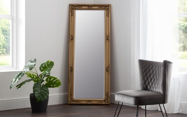 Gold-framed mirror on a white wall with a plant and chair in the foreground