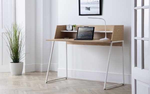 Modern desk with laptop, lamp, and plant in a minimalistic room.