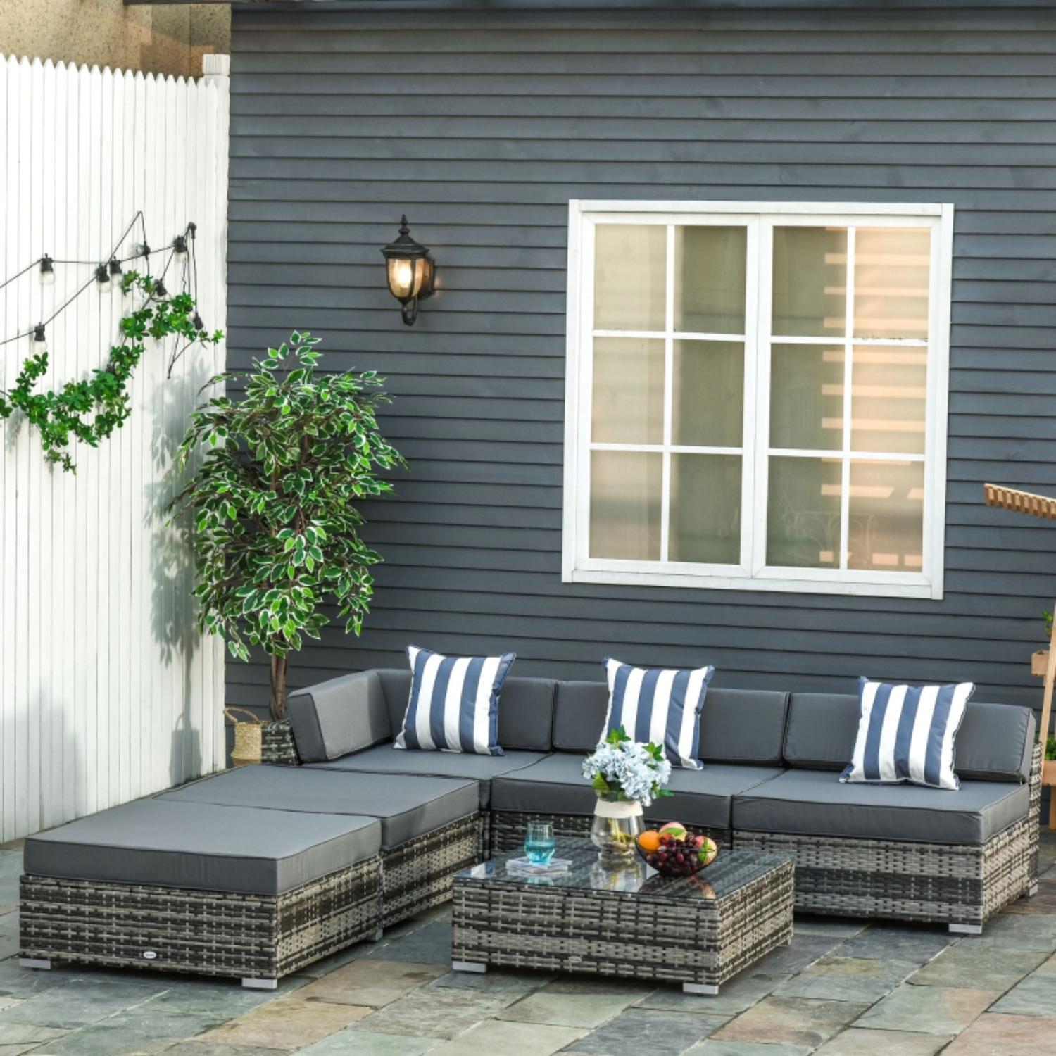 Outdoor patio set with gray cushions and striped pillows against a gray house exterior.