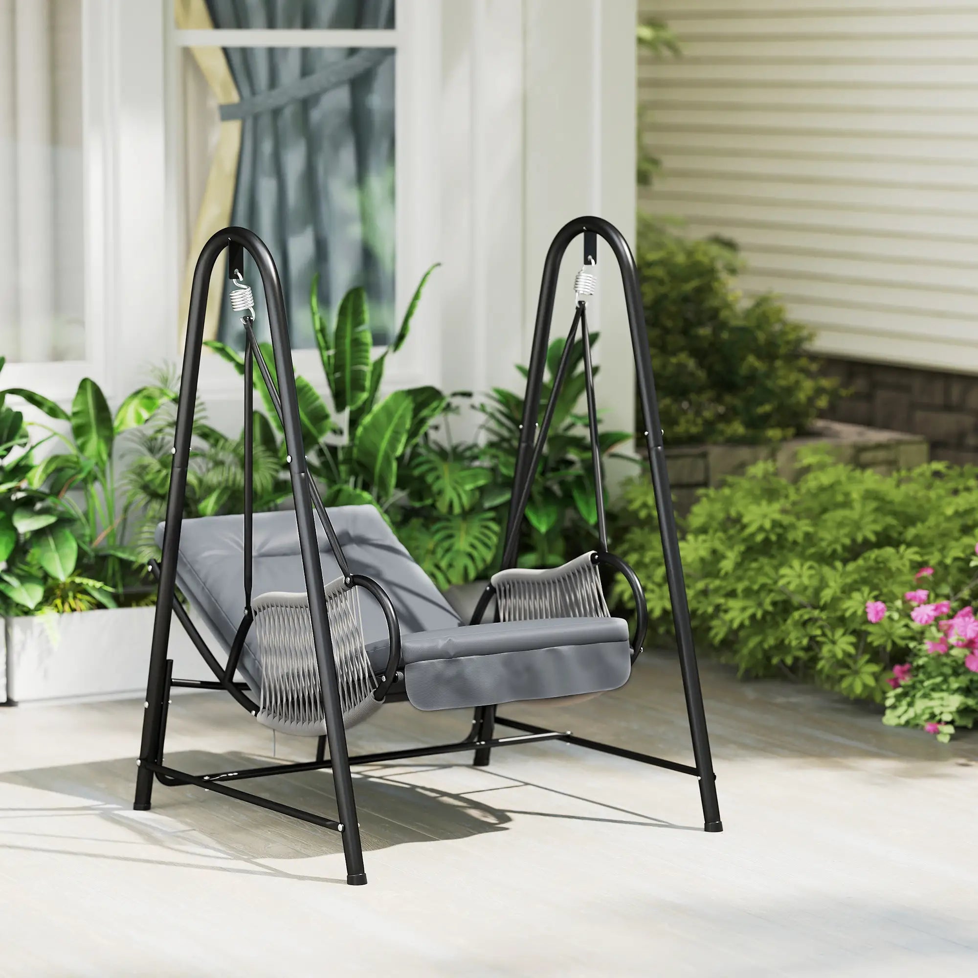 Gray swing chair with black metal frame on a patio with plants and flowers in the background