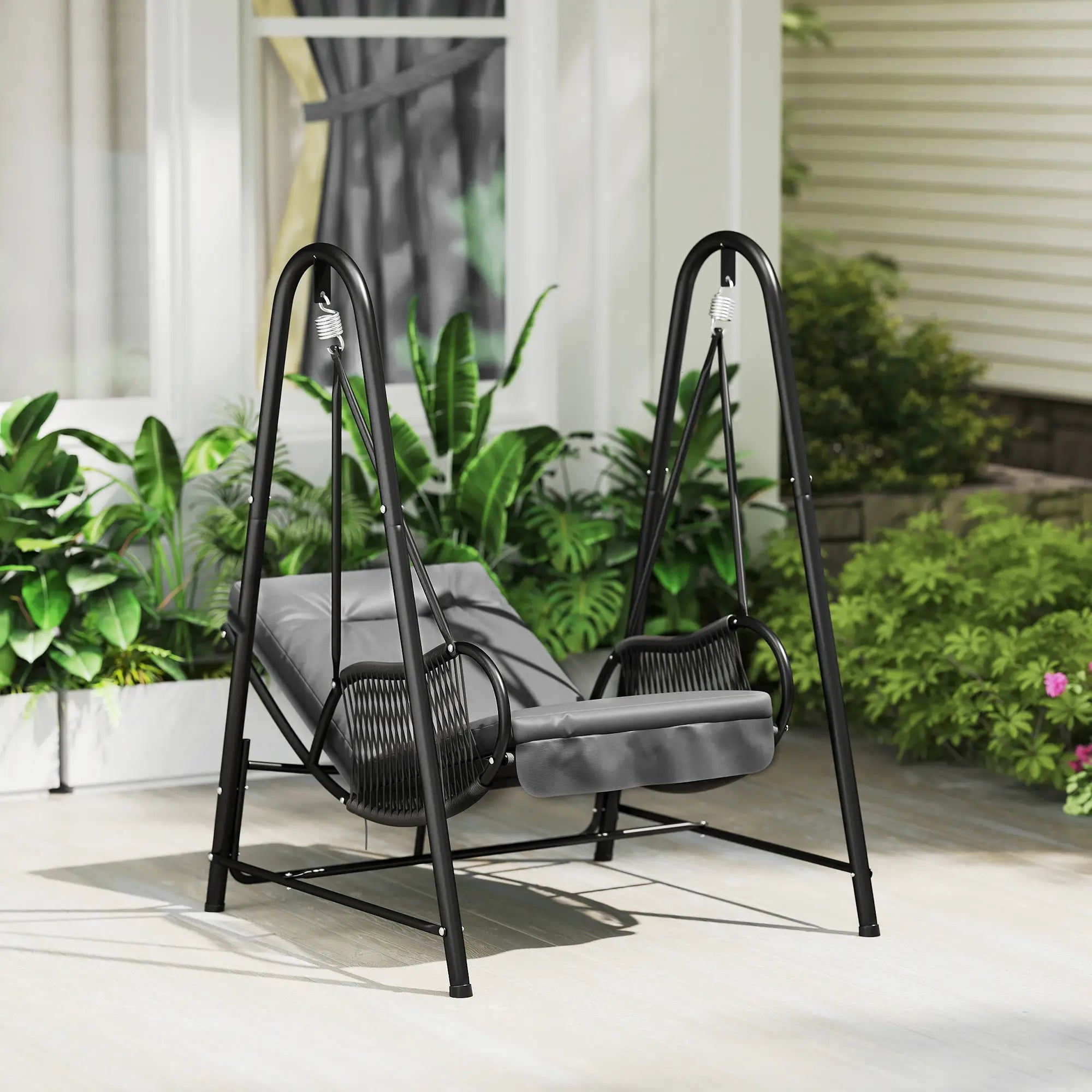 Gray swing chair with black metal frame on a patio with plants and a house in the background