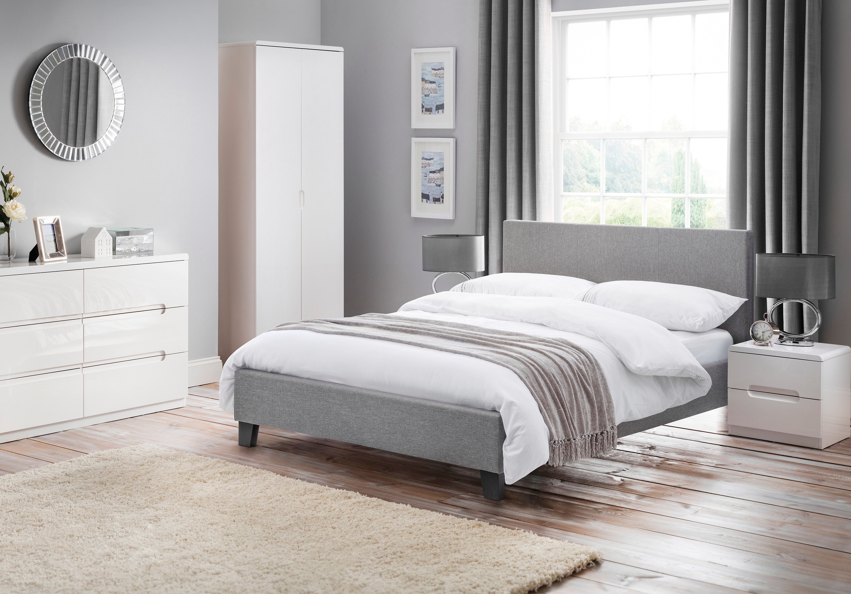 Modern bedroom with gray upholstered bed, white dresser, and window with curtains.