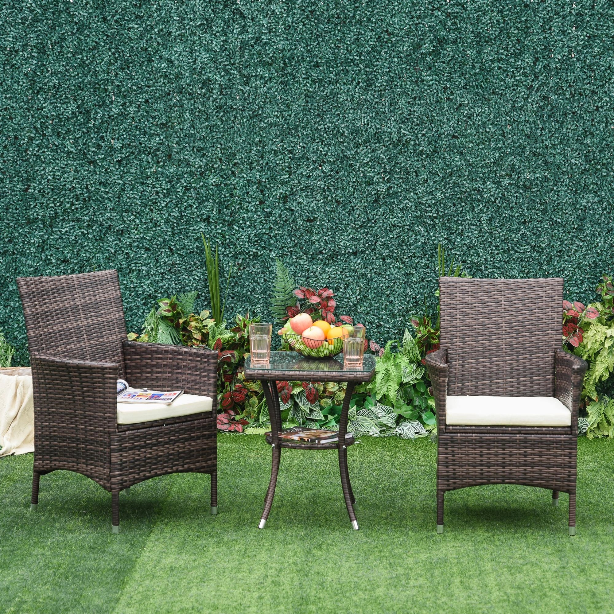 Two wicker chairs with cushions and a small table on a grassy area with a green wall background.