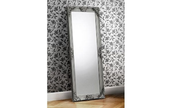 Decorative full-length mirror with ornate frame against a floral wallpapered wall.