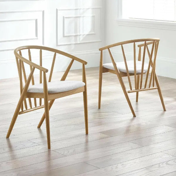 Two wooden chairs with white cushions on a light wooden floor.