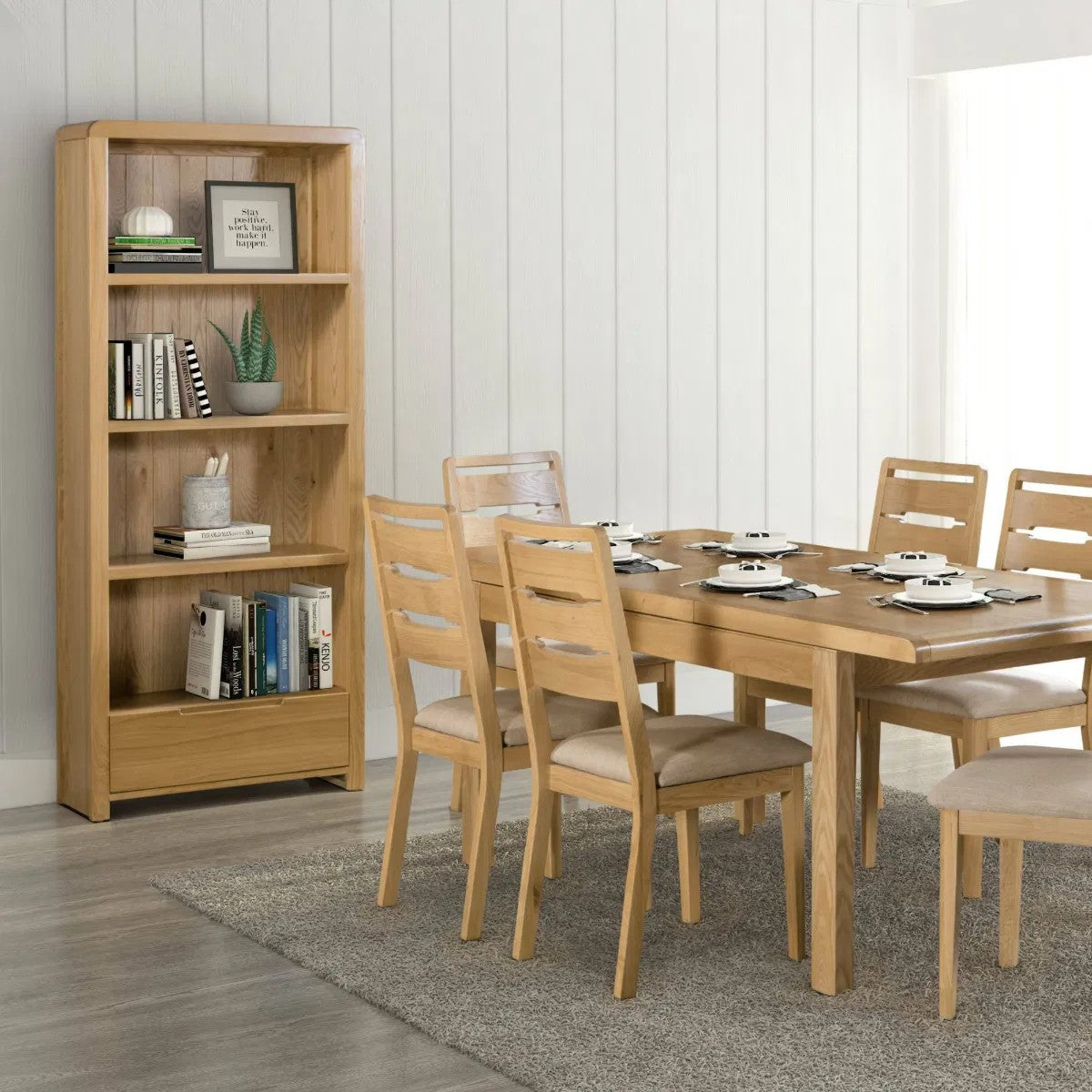 Wooden dining table with chairs and a bookshelf in a room with white walls.