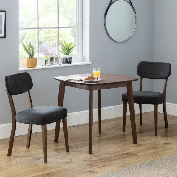Dining area with a small wooden table and two gray chairs in a room with a window and plants.
