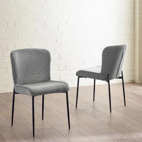Two gray chairs with black legs on a wooden floor against a white brick wall.
