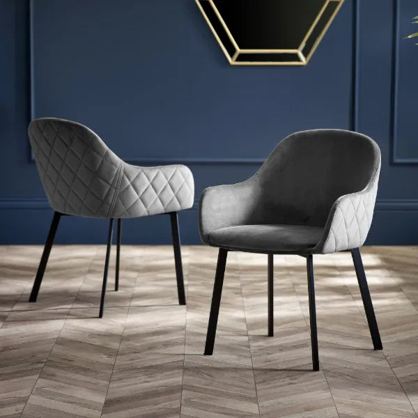 Two gray armchairs with quilted backrests on a wooden floor against a blue wall.