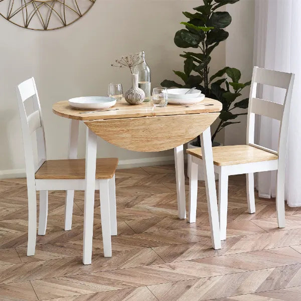 Dining area with a wooden drop-leaf table and white chairs on a herringbone wood floor.