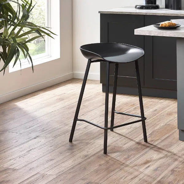 Black bar stool in a kitchen setting with a plant and countertop in the background.