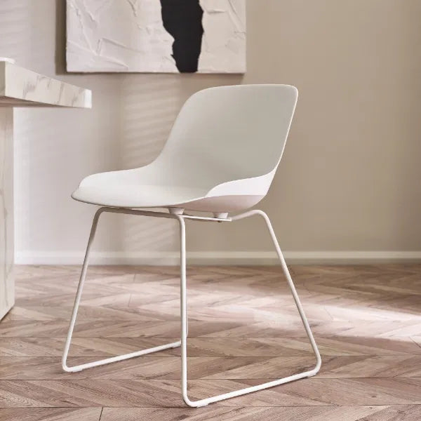 White chair on a wooden floor with a neutral wall and abstract art in the background