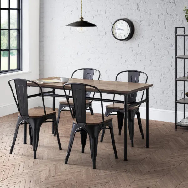 Dining area with wooden table and black metal chairs against a white brick wall.