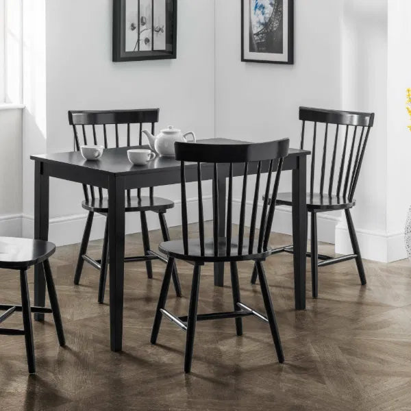 Black dining table with chairs in a room with white walls and wooden flooring.