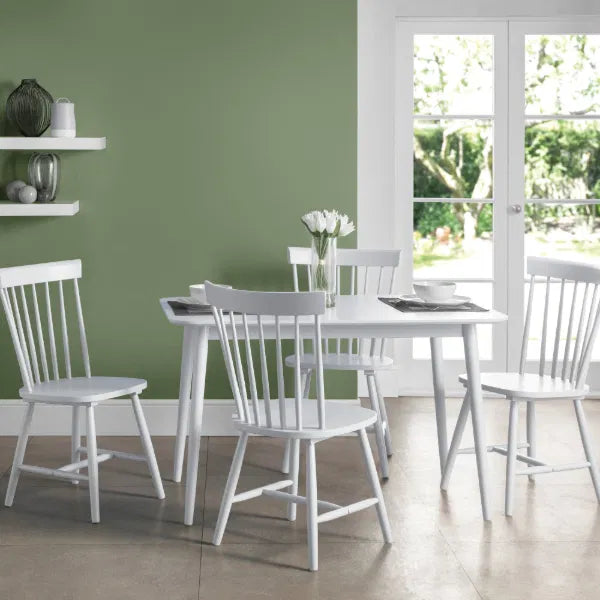Dining room with white table and chairs against a green wall.
