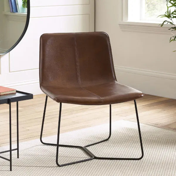 Brown leather chair with black metal legs in a room with a mirror and books on a table.